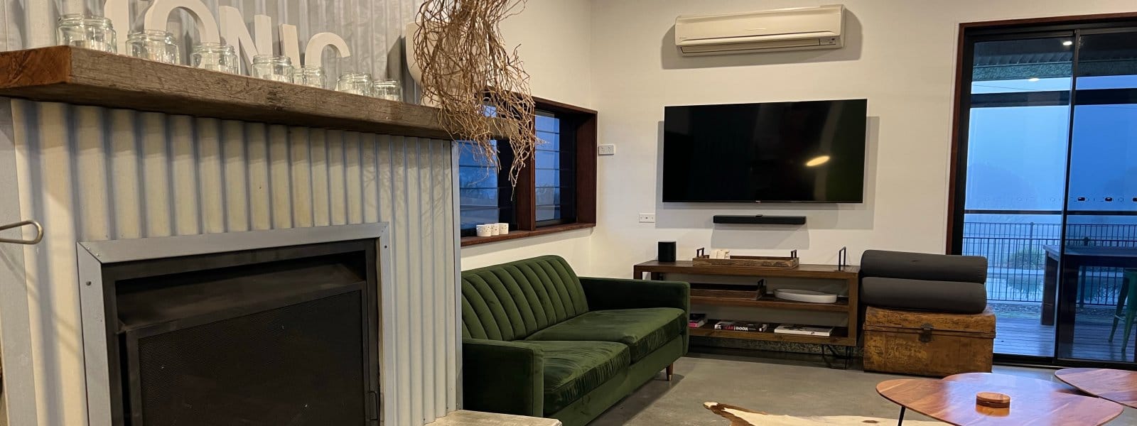 A lounge with a fireplace, green sofa and doors to the deck
