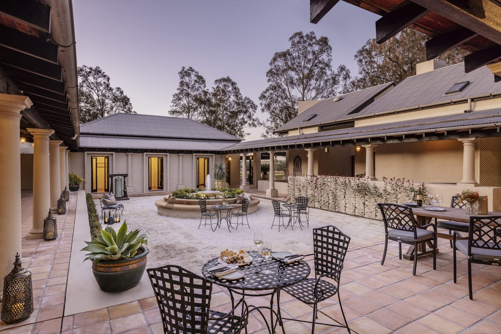 Lodge courtyard at dusk with fountain, iron tables and lantern-lit colonnade at Tower Lodge, Pokolbin, Hunter Valley