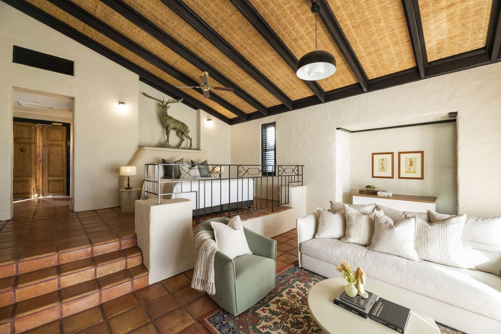 A suite living room with a raised bed platform under a thatched and beamed ceiling
