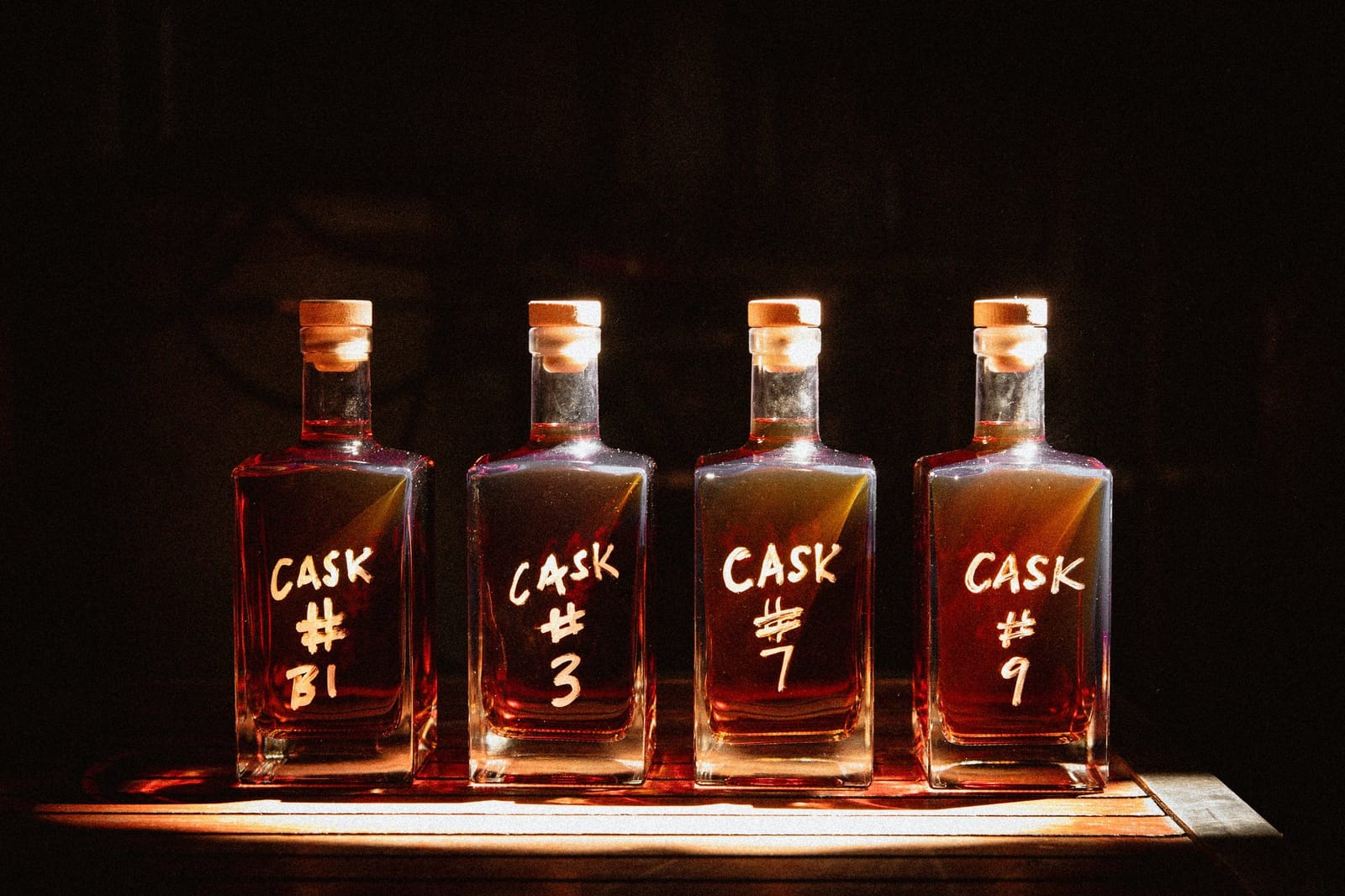 Four whiskey bottles with gold caps and cask numbers on black