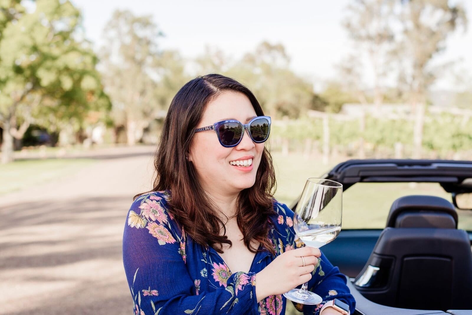 Woman enjoying white wine in convertible overlooking vineyard