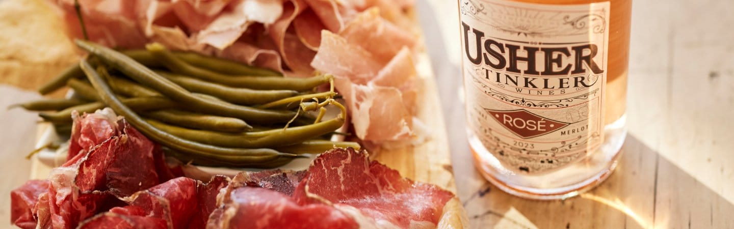Charcuterie board of prosciutto and green beans beside a bottle of Usher Tinkler wine