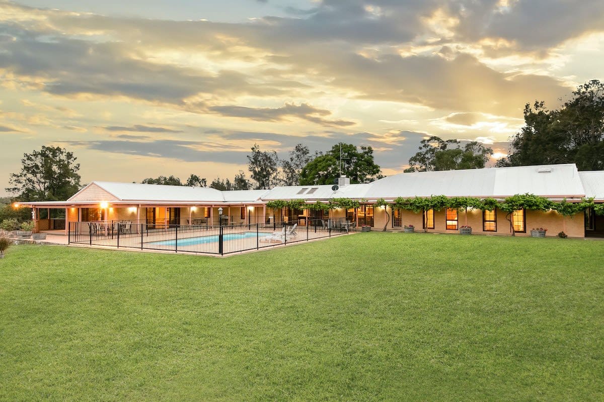 Homestead lit at dusk with vine-covered verandah, fenced pool and wide lawn at Villa Vigneto, Pokolbin, Hunter Valley