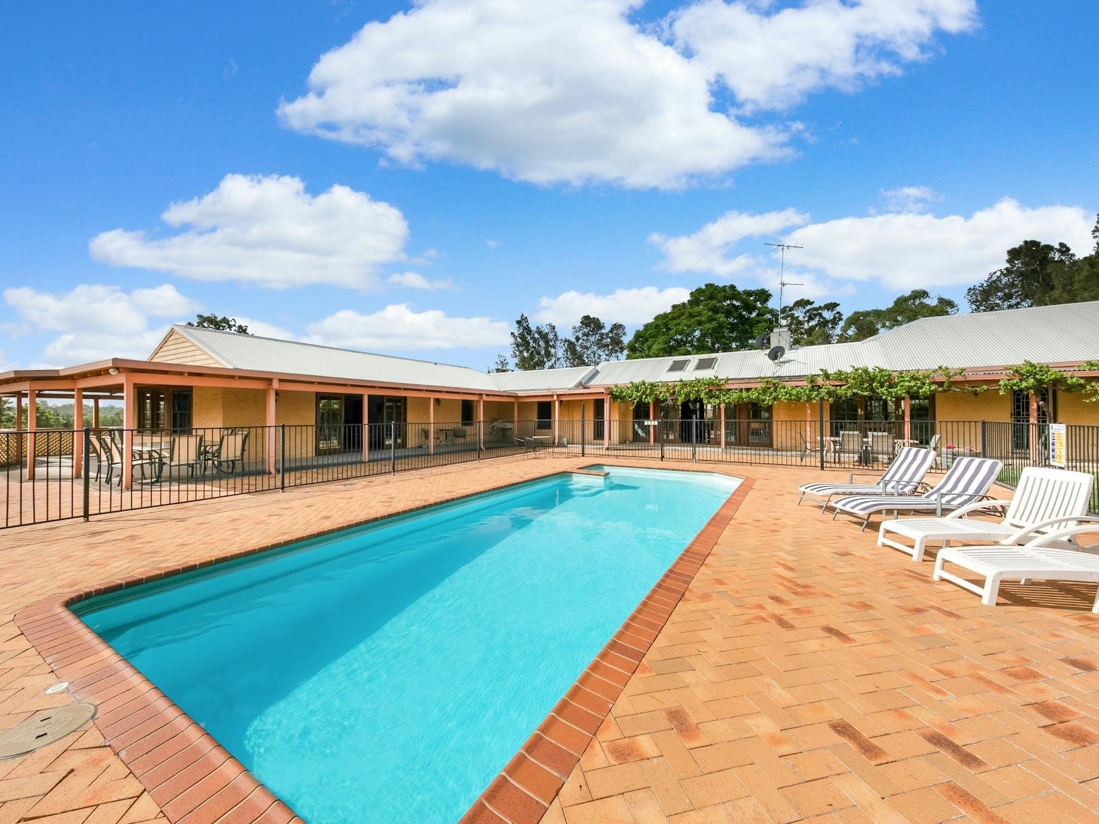 The fenced swimming pool and sun loungers along the verandah of the homestead