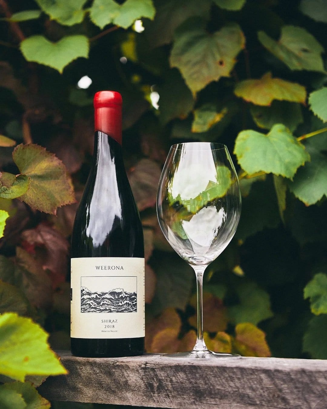 A bottle of Weerona 2018 Hunter Valley Shiraz beside an empty glass on a timber rail