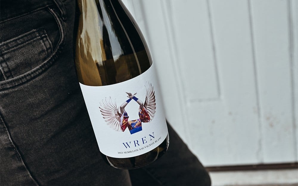 A bottle of Wren Semillon Sauvignon Blanc held against a white timber wall