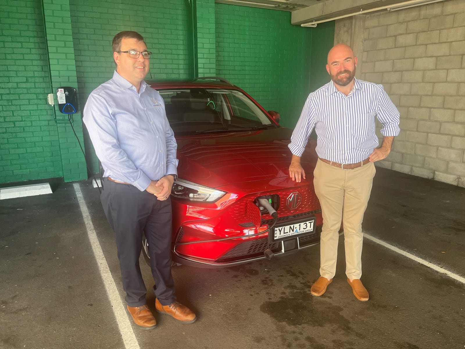 Two men with red electric vehicle at charging station