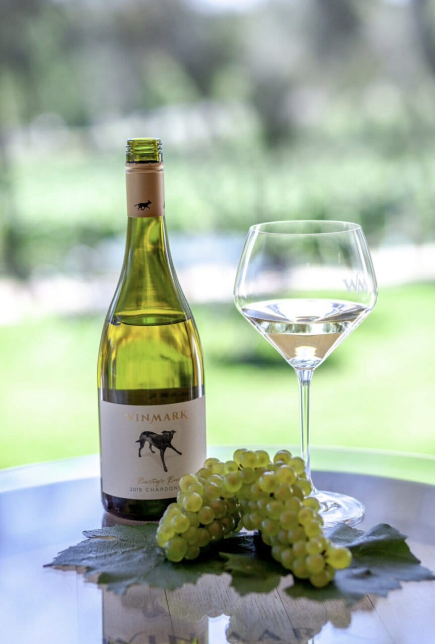 Winmark chardonnay bottle with wine glass and grapes on table