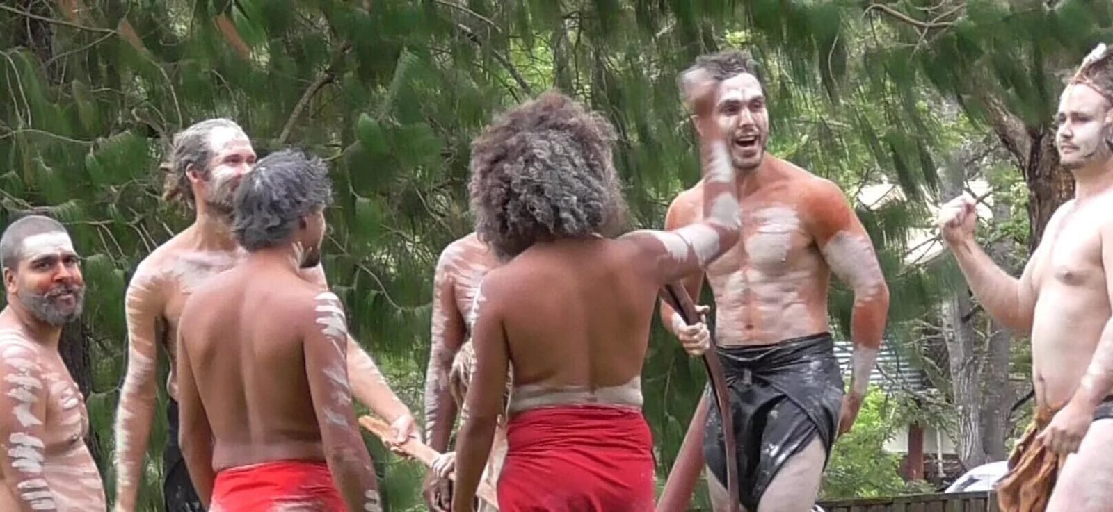 Indigenous cultural gathering with participants displaying traditional body art designs outdoors