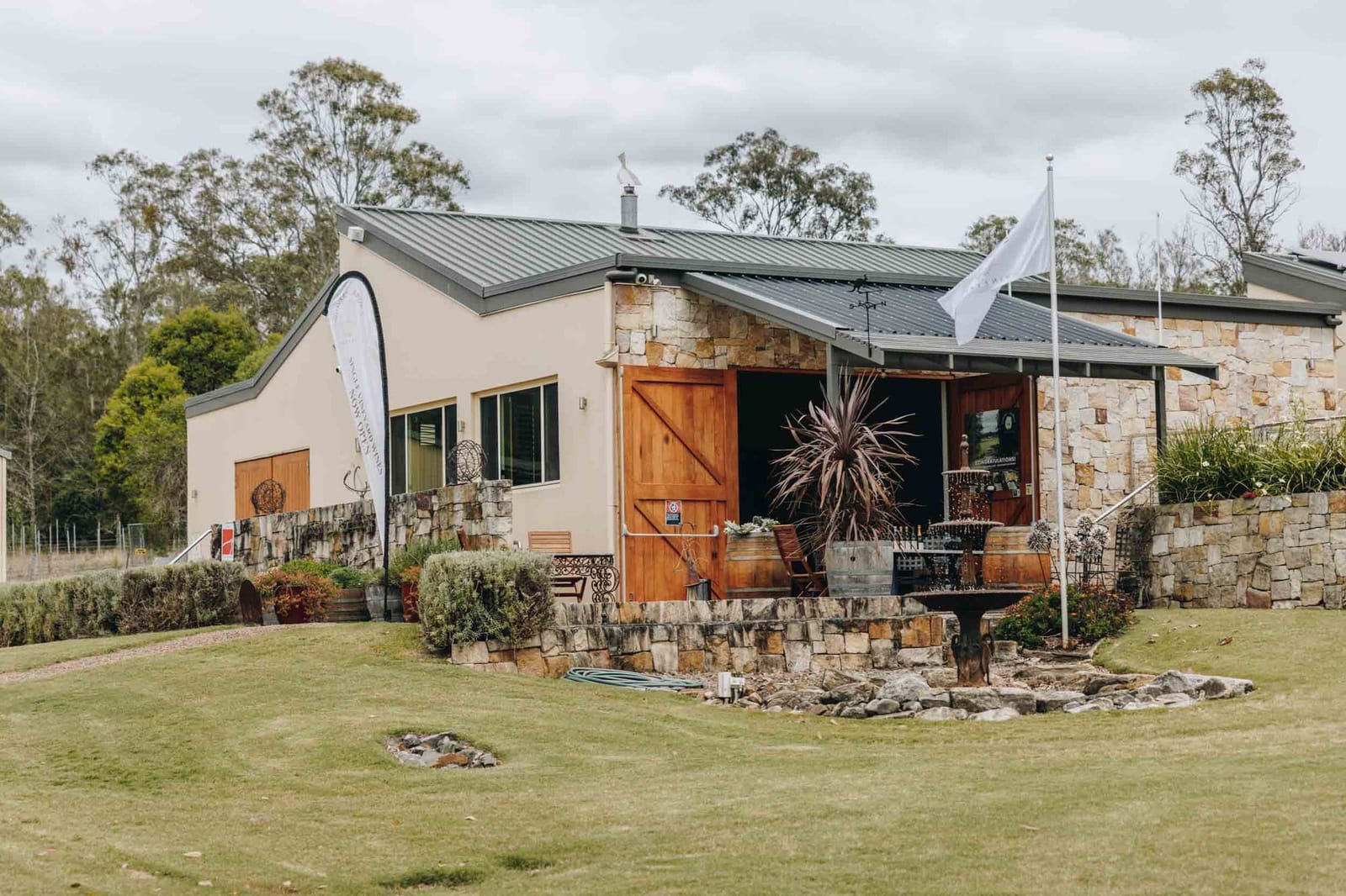 Stone and render cellar door with timber barn doors seen across lawn at Wombat Crossing, Pokolbin, Hunter Valley