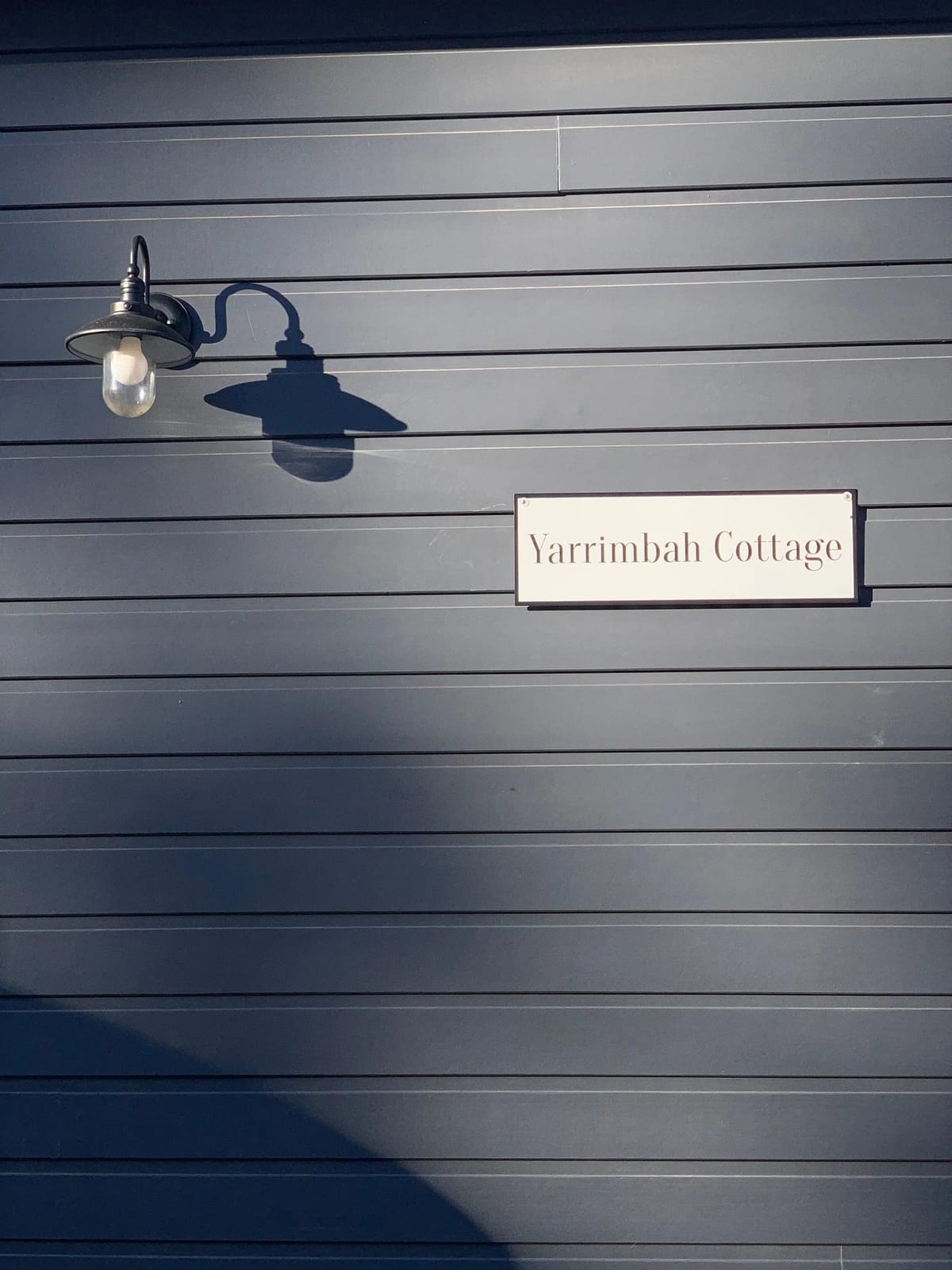 The Yarrimbah Cottage name plate mounted on the dark cottage cladding, beside an outdoor light