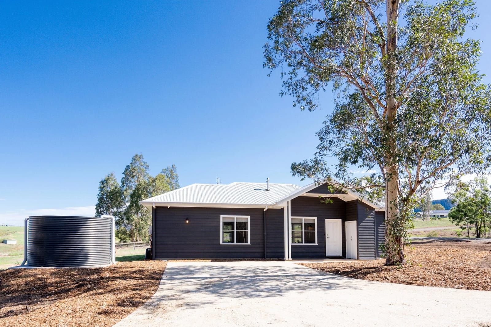 Dark-clad off-grid cottage with rainwater tank set among gum trees at Yarrimbah Cottage, Pokolbin, Hunter Valley