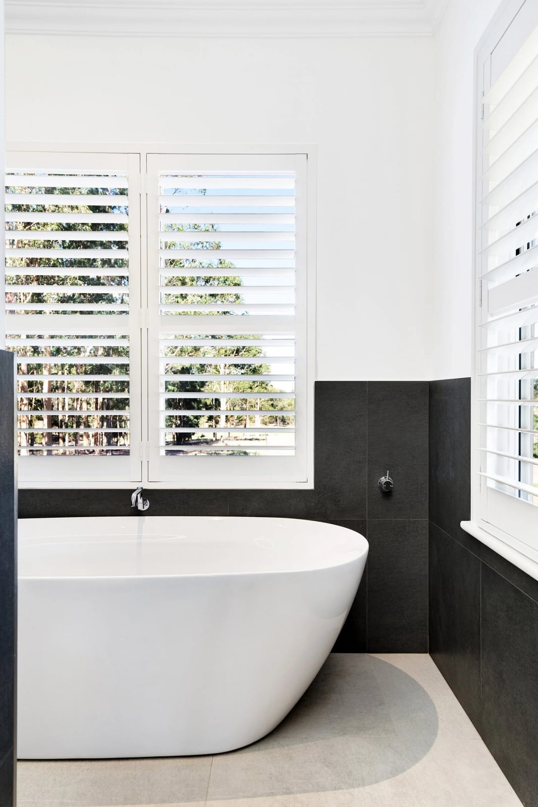The freestanding bath below plantation shutters looking out to gum trees and paddock